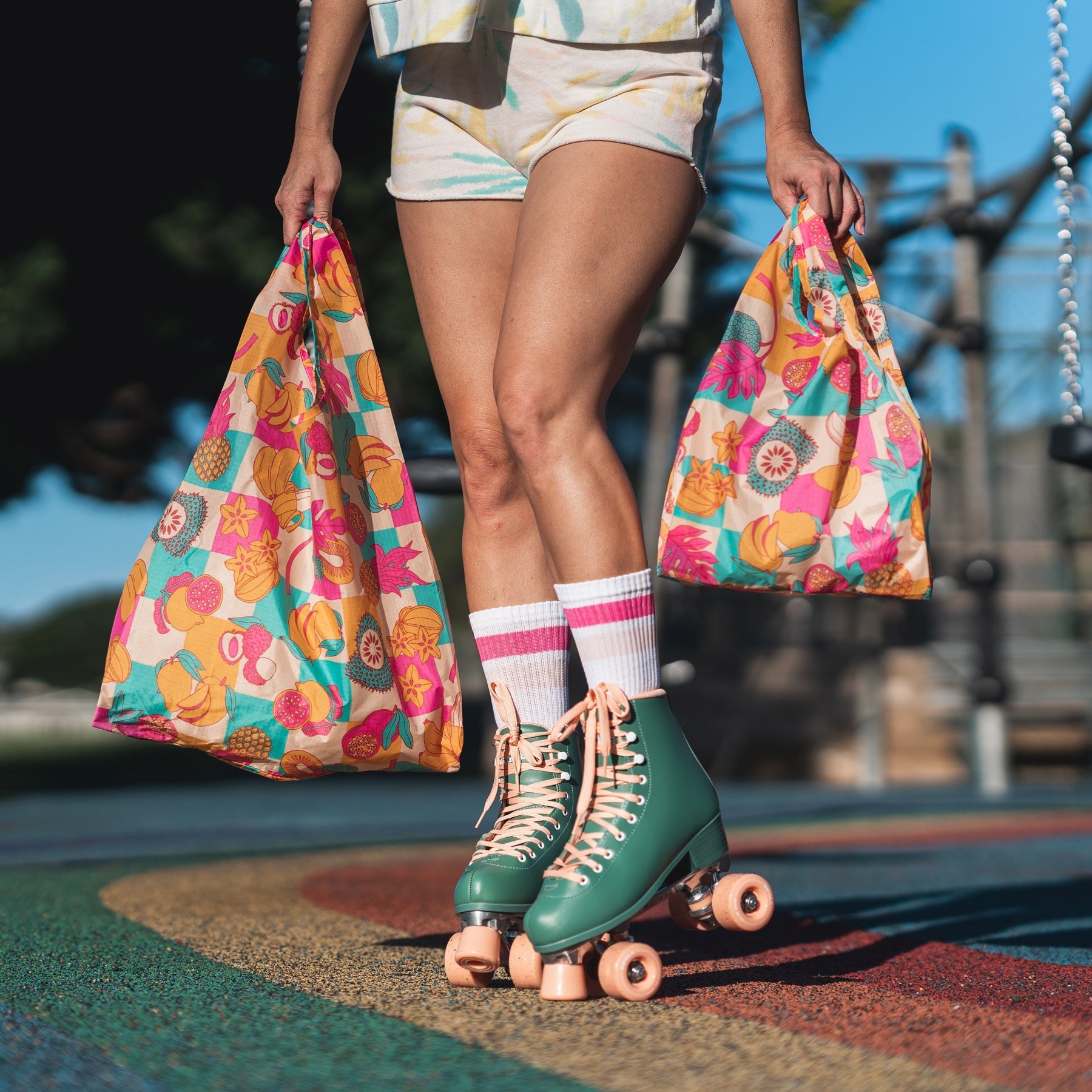 Jana Lam rollerskates holding baggu collab reusuable bags in Fruit Stand print tropical fruits and checkerboard